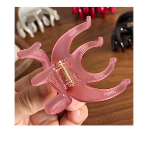 Close-up of a pink acetate hair claw with a gold spring mechanism on a wooden background