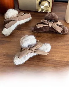 Detail view of plush bow claw clips in beige, dark brown, and grey on a wooden desk