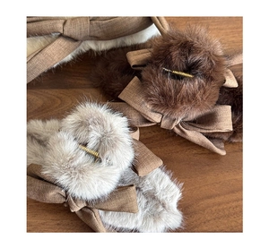 Detailed close-up of plush faux fur bow hair claws in brown and grey on a wood surface