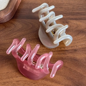 Elegant cream and pink acetate hair claws with gold label on vintage wood background