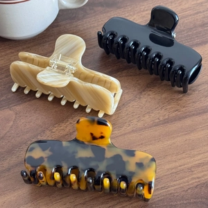 Three elegant French acetate hair claws in black, marble, and tortoise shell on wood
