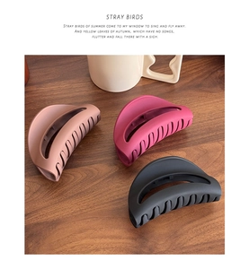 Detailed view of matte silicone hair claws in beige, rose red, and black on a wooden desk