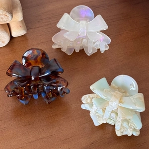Three elegant acetate bow hair claws in pearly white, tortoiseshell, and marble cream finishes