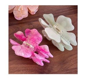 Detailed macro view of acetate flower hair clips in pink and mint green with small rhinestones