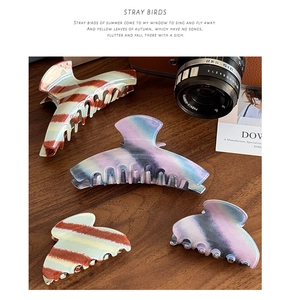 Close-up of acetate claw clips in striped and marble patterns on a dark wood background