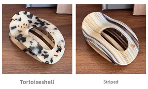 Detail of tortoiseshell and striped acetate hair clips with gold logo on wood