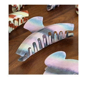 Macro detail of large acetate hair claw clip with pearlescent finish on dark wood table