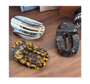 Three acetate hair clips with marble and tortoise patterns on a vintage wooden desk