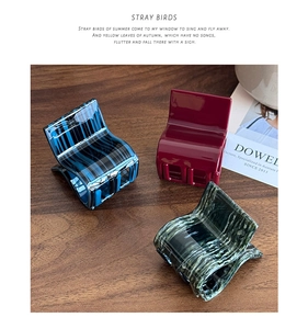 Three acetate hair claws with marble and stripe textures on a rustic wooden background