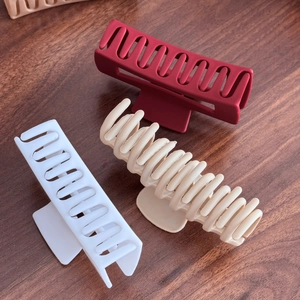 Three-piece set of large matte hair claws in red and white on a wooden surface