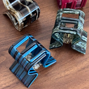 Textured acetate square hair claws in marble and striped patterns on a wood surface