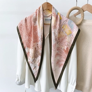 Detail of tropical leaf print silk scarf draped on a white shirt and wooden hanger
