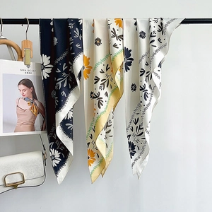 Elegant floral print silk scarves in navy, beige, and yellow colors hanging on a rack