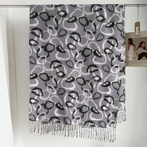 Detail shot of a soft gray pashmina scarf featuring abstract line print and fine fringe trim