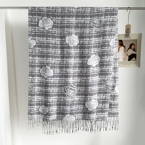 Détail d'un châle à carreaux gris avec fleurs de camélia blanches et franges élégantes