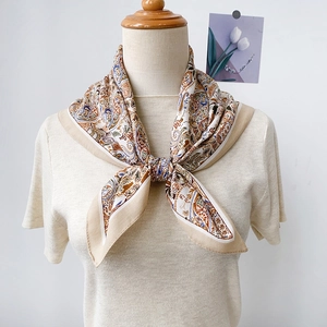 Gros plan d'un foulard beige à motif paisley noué sur un haut en maille style rétro