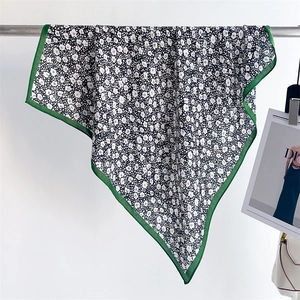 Floral square silk scarf with green border hanging on metal rod against white wall