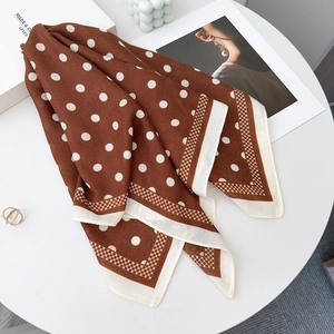 Detail of silk-feel brown polka dot scarf with geometric pattern border on white desk