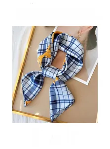 Gros plan d'un foulard carré soyeux à carreaux et motifs oranges sur plateau doré