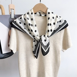 Close-up of black and white polka dot silk scarf styled on a beige knitted sweater