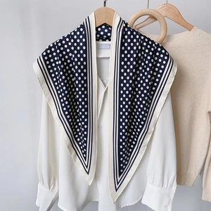 Detail of navy blue polka dot scarf with white trim on wooden hanger for outfit styling