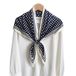 Navy blue polka dot silk scarf tied on a white chiffon shirt displayed on a hanger