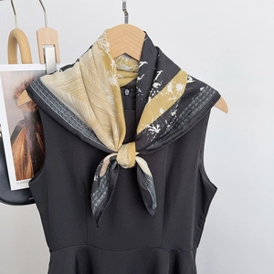Détail d'un carré de soie et laine noué en nœud sur une robe noire, imprimé jaune
