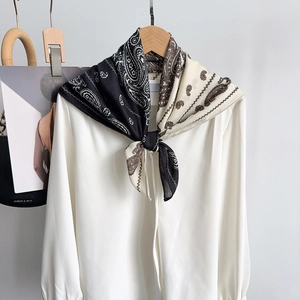 Dettaglio di un foulard in seta con motivo paisley annodato nei toni nero beige e marrone