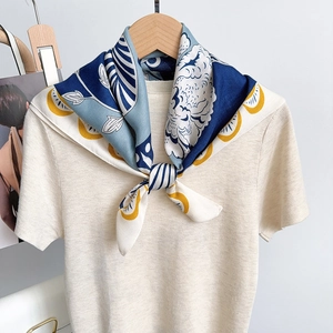 Floral printed silk scarf tied on a beige sweater featuring blue and yellow patterns