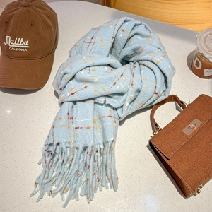 Detail of light blue plaid cashmere-like scarf with fringe on a marble texture surface