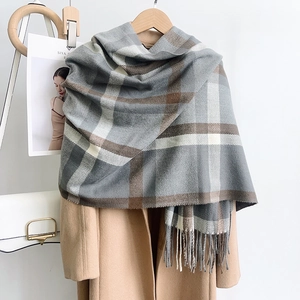 Detail of plaid scarf texture with tassels layered on a camel coat and magazines
