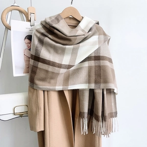 Detail of earthy plaid scarf with tassel edges paired with a classic camel wool coat