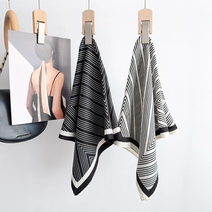 Elegant black and white striped silk square scarf hanging on a wooden clip with soft lighting