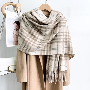 Detail view of the thick plaid scarf with tassels styled on a camel wool winter coat