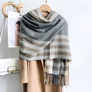 Détail d'une écharpe à carreaux gris et beige avec franges sur un manteau en laine