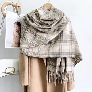 Detail of premium beige plaid cashmere-like scarf with soft tassels on a camel coat