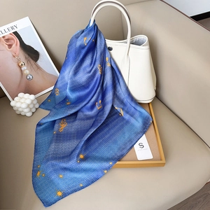 Navy blue silk scarf with yellow musical note patterns draped over a stylish white leather bag
