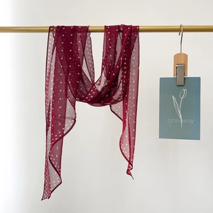 Elegant burgundy silk scarf with white polka dots hanging on a gold wooden rod