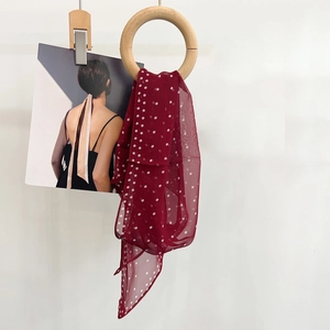 Close-up of a burgundy polka dot silk scarf draped through a wooden ring on white background