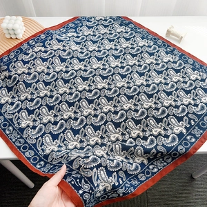 Close-up of a navy paisley square silk scarf with red edges showing smooth fabric texture