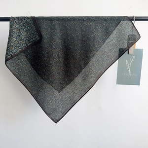 Close-up of a dark green paisley silk scarf draped on a metal rack with hem details