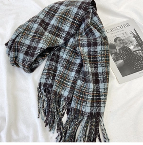 Close-up of thick plaid scarf texture with orange and blue fringe detail on white fabric