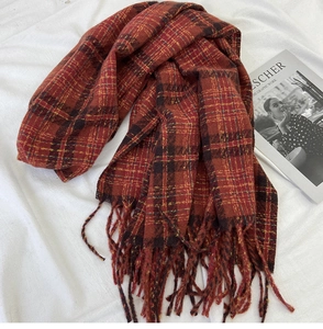 Detailed flat lay of a red plaid tassel scarf with a warm cashmere-like texture and fringed edges