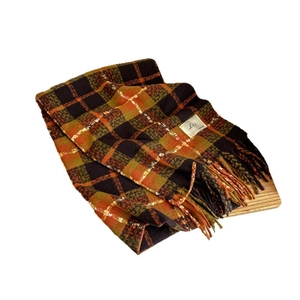 Plaid scarf with brown orange olive check pattern and tassel trim on wooden tray