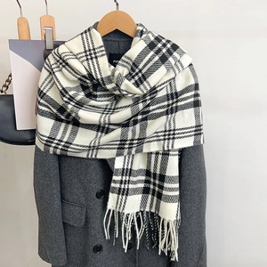 Close-up detail of soft plaid scarf with fringe tassels on grey coat background