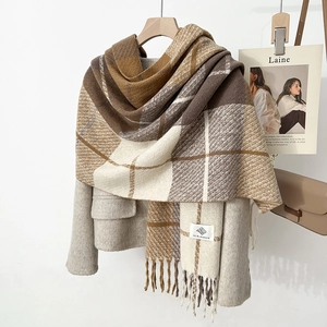 Close-up of thick plaid wool scarf with fringe and brand label on a beige coat