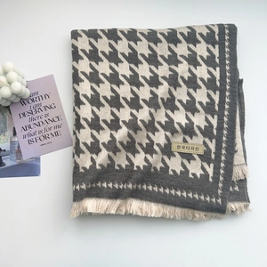 Detail of grey houndstooth scarf featuring soft fringes and a stylish textile label