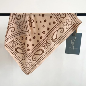 Beige and brown paisley pattern silk square scarf hung on a black metal bar