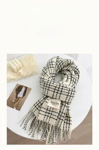 Detail of soft black and white plaid scarf with fringe and brand label on a white table