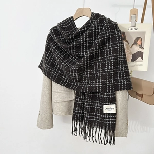 Detail view of brown checkered scarf with fringe on a beige blazer and wooden hanger